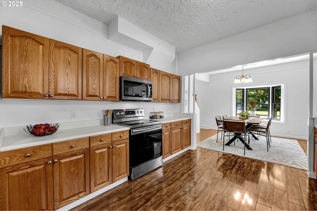 6206 N Denver Ave, Portland, OR 97217 - kitchen with appliances with stainless steel finishes, brown cabinets, a chandelier, a textured ceiling, and dark wood-type flooring