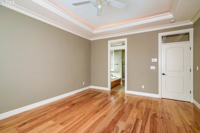 unfurnished bedroom with ornamental molding, connected bathroom, light hardwood / wood-style floors, and a tray ceiling