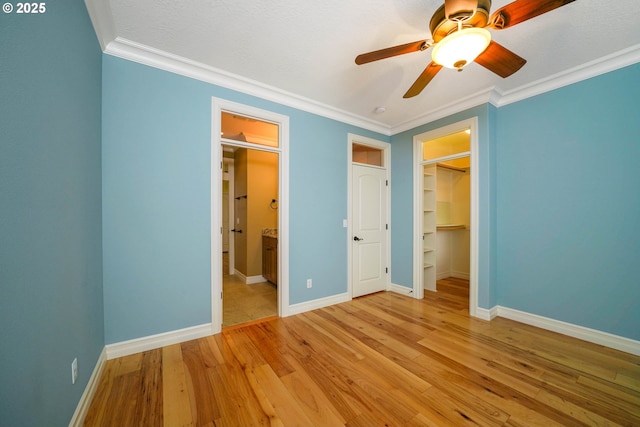 unfurnished bedroom with a walk in closet, ornamental molding, a closet, and light wood-type flooring