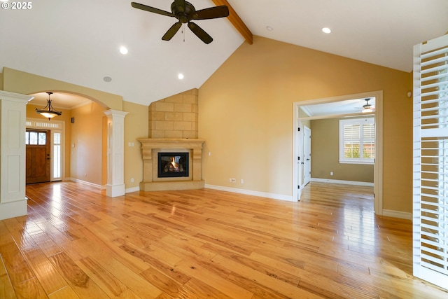 unfurnished living room featuring light hardwood / wood-style flooring, a large fireplace, beamed ceiling, and ornate columns