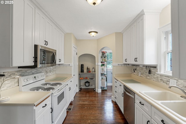 1825 NE 4th St, Salem, OR 97301 - kitchen with stainless steel appliances, arched walkways, dark wood-style flooring, white cabinets, and tasteful backsplash
