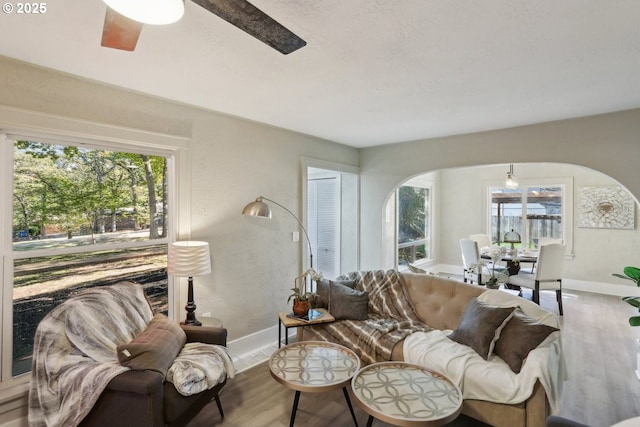 living area featuring arched walkways, wood finished floors, a ceiling fan, and baseboards