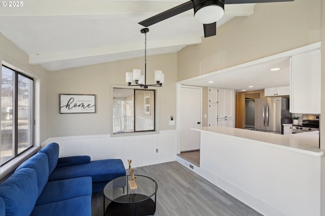 living room with ceiling fan with notable chandelier, a wainscoted wall, vaulted ceiling with beams, and wood finished floors