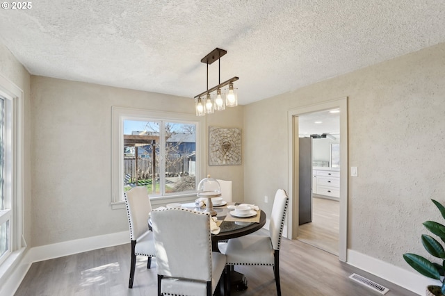 dining area with visible vents, a textured wall, a textured ceiling, and wood finished floors