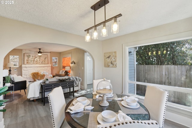 dining room with arched walkways, a wealth of natural light, ceiling fan, a textured ceiling, and wood finished floors