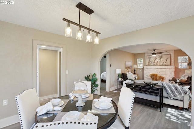 dining room with baseboards, arched walkways, a ceiling fan, wood finished floors, and a textured ceiling