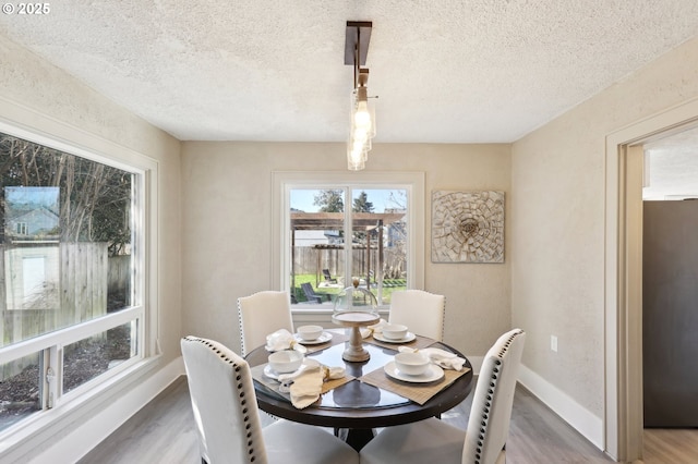 dining area featuring a textured ceiling, baseboards, and wood finished floors