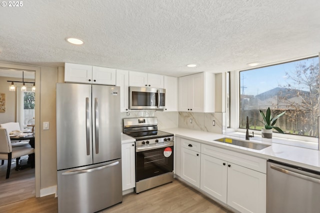 kitchen featuring stainless steel appliances, light countertops, white cabinets, and a sink