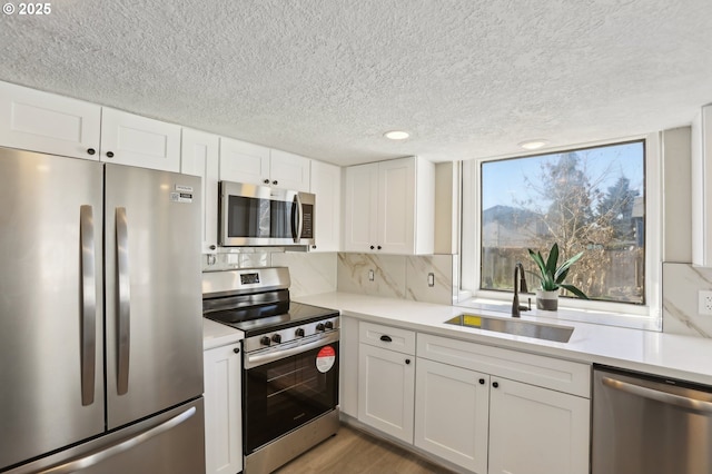 kitchen featuring tasteful backsplash, white cabinets, stainless steel appliances, light countertops, and a sink