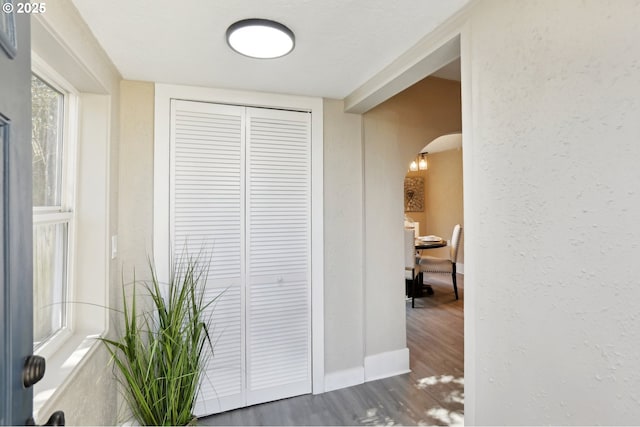 corridor with arched walkways, a textured wall, baseboards, and wood finished floors