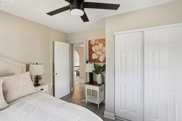 bedroom featuring arched walkways, dark wood-type flooring, a ceiling fan, baseboards, and a closet