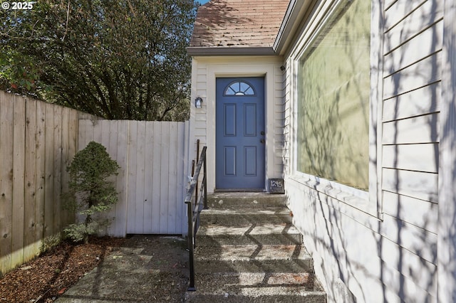 entrance to property featuring a shingled roof and fence