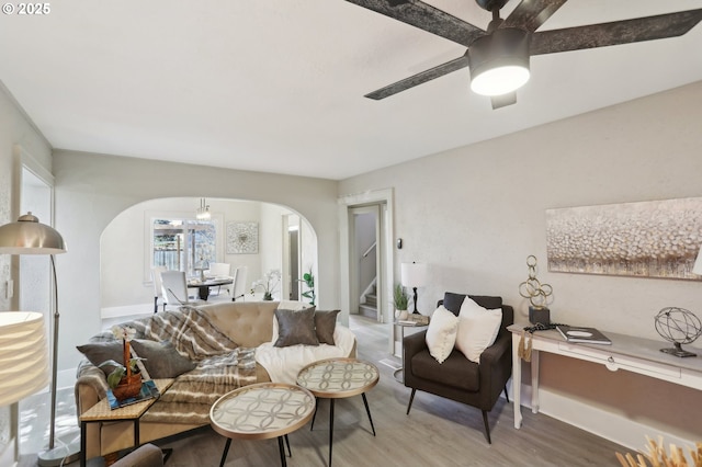 living area featuring a ceiling fan, stairs, arched walkways, and wood finished floors