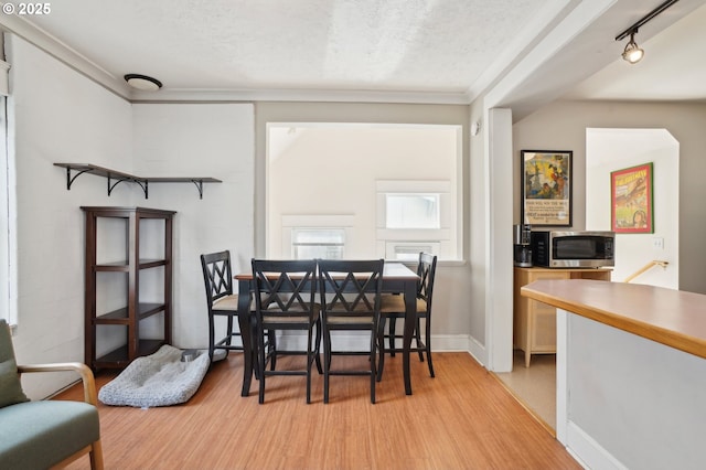 dining room with a textured ceiling, crown molding, and light wood finished floors