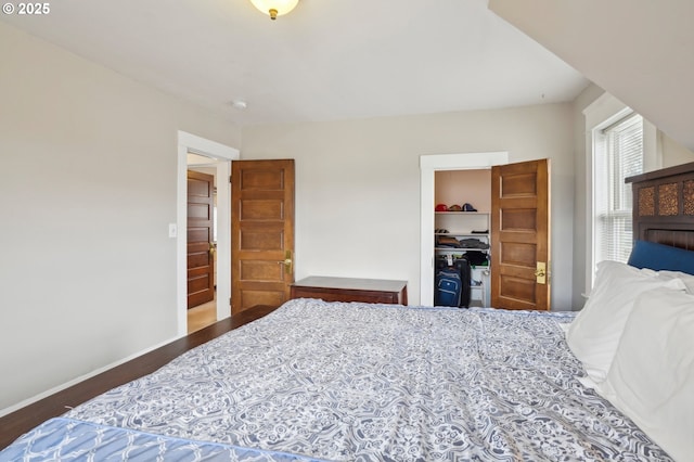 bedroom with a closet, a spacious closet, baseboards, and wood finished floors