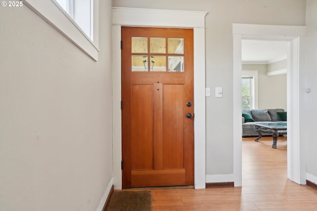 foyer with crown molding, baseboards, and light wood finished floors