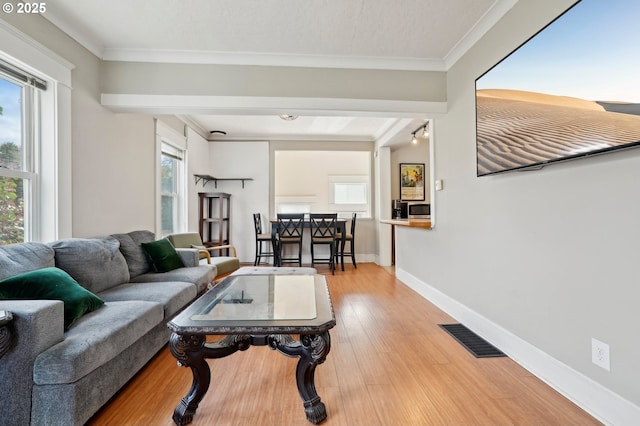 living room featuring visible vents, baseboards, light wood finished floors, and ornamental molding