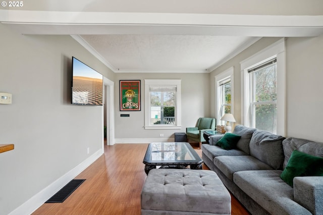 living room featuring ornamental molding, baseboards, visible vents, and light wood-type flooring