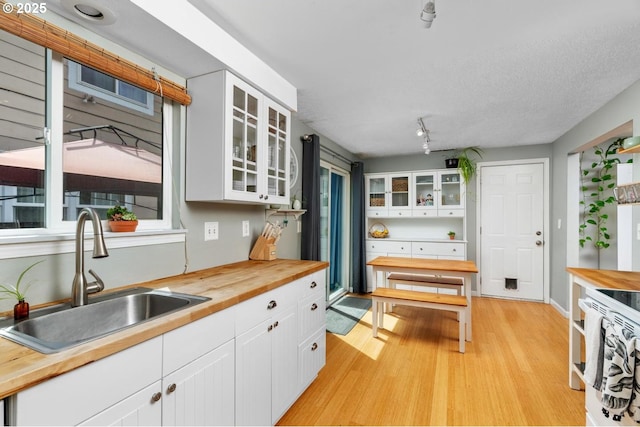 kitchen with butcher block counters, a sink, light wood-style flooring, and white cabinets