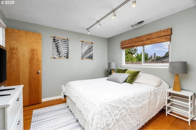bedroom with light wood finished floors, a textured ceiling, and baseboards
