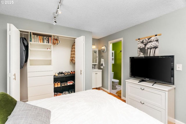 bedroom with baseboards, ensuite bathroom, and a textured ceiling