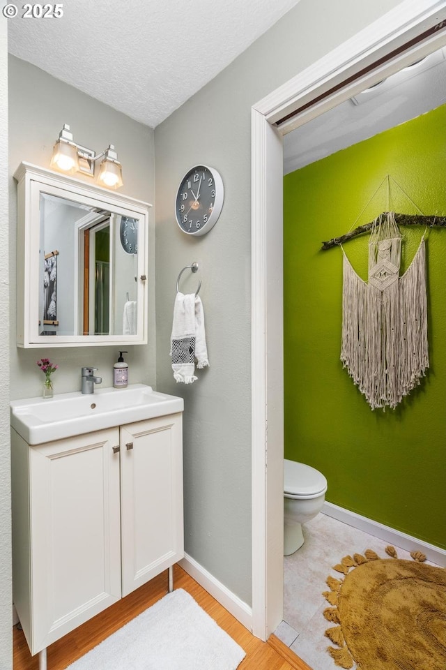 bathroom featuring toilet, vanity, baseboards, wood finished floors, and a textured ceiling