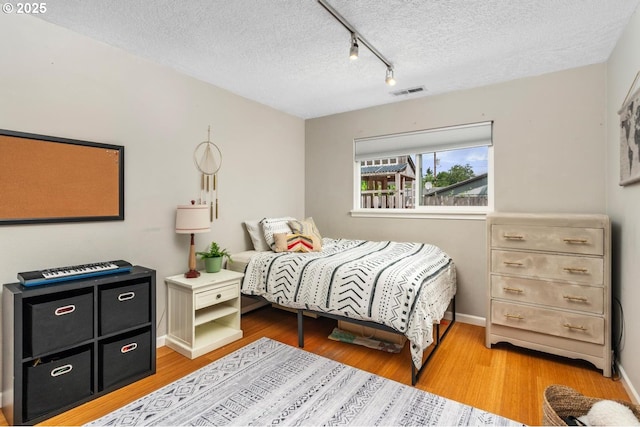 bedroom featuring track lighting, a textured ceiling, wood finished floors, and baseboards