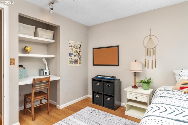 bedroom featuring light wood-type flooring, baseboards, and a textured ceiling