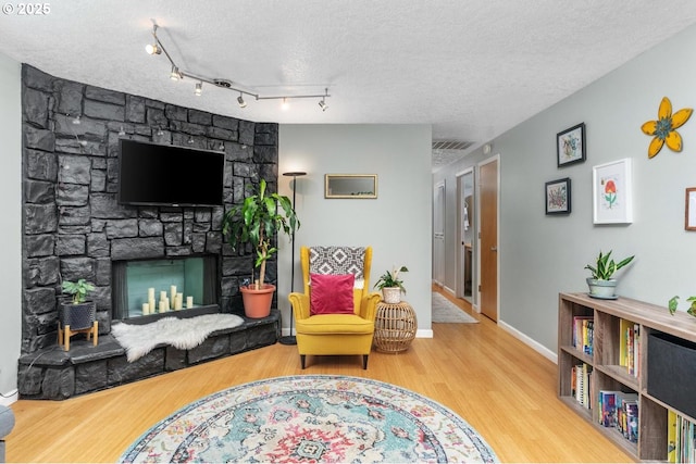 living area featuring wood finished floors, a textured ceiling, a fireplace, and baseboards