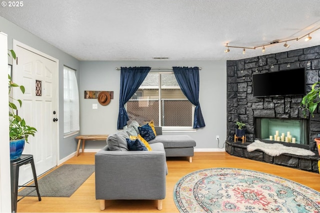 living area featuring a textured ceiling, wood finished floors, a stone fireplace, and baseboards