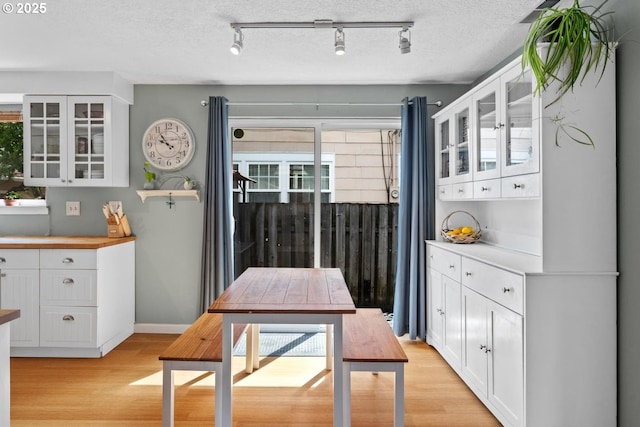 kitchen with light wood-type flooring, white cabinets, rail lighting, and a textured ceiling