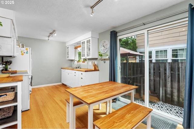 kitchen with rail lighting, white appliances, white cabinets, light wood-style flooring, and a textured ceiling