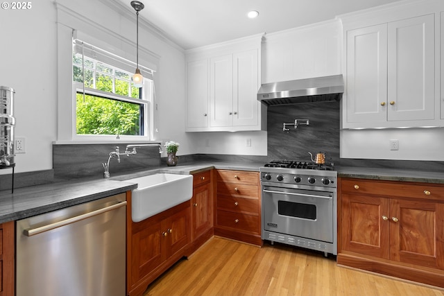 kitchen featuring white cabinetry, wall chimney exhaust hood, stainless steel appliances, and a sink