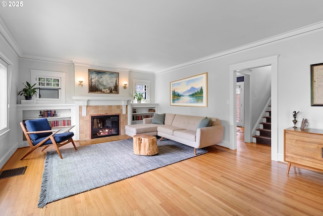 living area featuring visible vents, wood finished floors, a fireplace, and ornamental molding