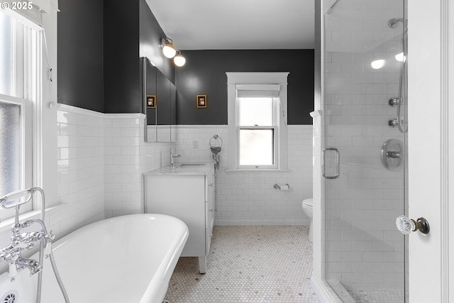 bathroom featuring a stall shower, tile walls, wainscoting, vanity, and a freestanding bath