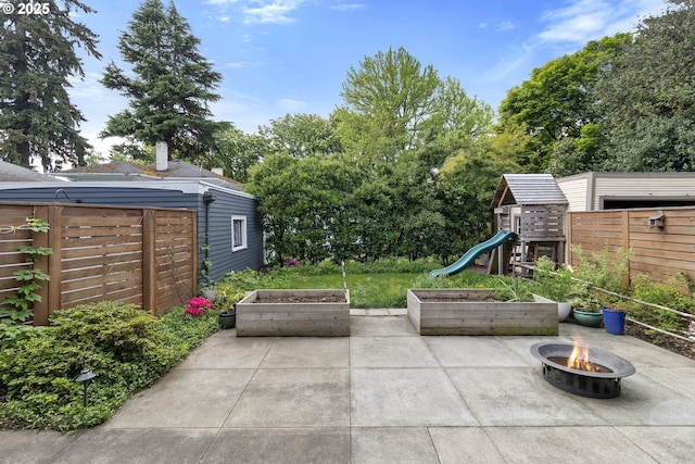 view of patio / terrace featuring an outdoor fire pit, a vegetable garden, a playground, and fence