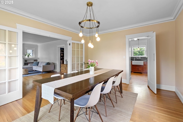 dining area with an inviting chandelier, ornamental molding, baseboards, and light wood-style floors
