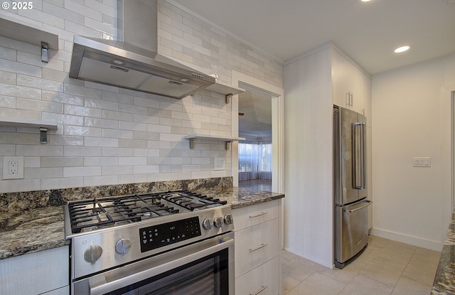 kitchen with stainless steel appliances, dark stone countertops, wall chimney range hood, and decorative backsplash