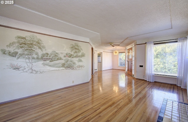 empty room with ceiling fan, a healthy amount of sunlight, wood-type flooring, and a textured ceiling