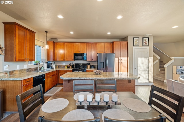 kitchen with black appliances, a kitchen island, brown cabinets, and a sink