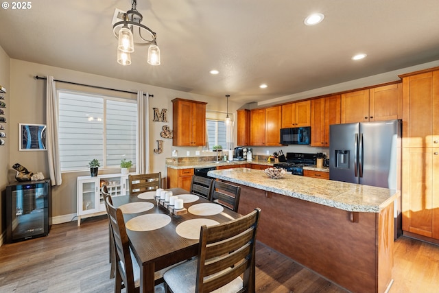 kitchen with brown cabinets, wood finished floors, black appliances, a sink, and recessed lighting