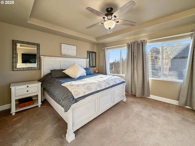 carpeted bedroom featuring a tray ceiling, ceiling fan, and baseboards