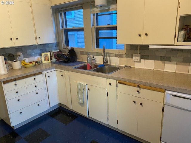 kitchen featuring white dishwasher, decorative backsplash, white cabinetry, and sink