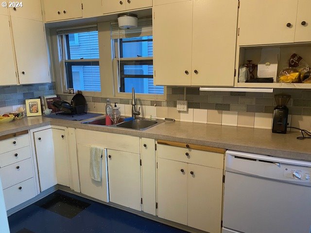 kitchen featuring white dishwasher, decorative backsplash, white cabinetry, and sink