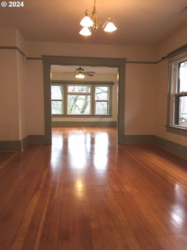 spare room featuring a healthy amount of sunlight, wood-type flooring, and ceiling fan with notable chandelier