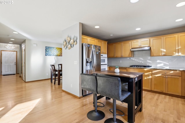 kitchen with appliances with stainless steel finishes, light hardwood / wood-style flooring, light brown cabinets, and decorative backsplash