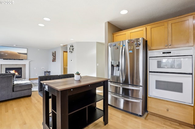 kitchen featuring a tiled fireplace, stainless steel fridge, white double oven, and light hardwood / wood-style flooring