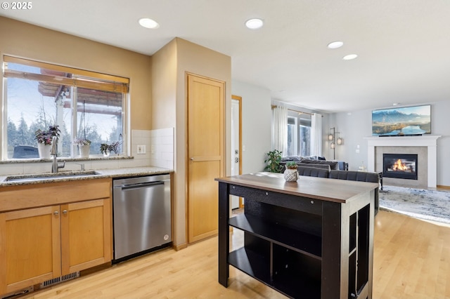 kitchen featuring a fireplace, tasteful backsplash, dishwasher, sink, and light hardwood / wood-style flooring