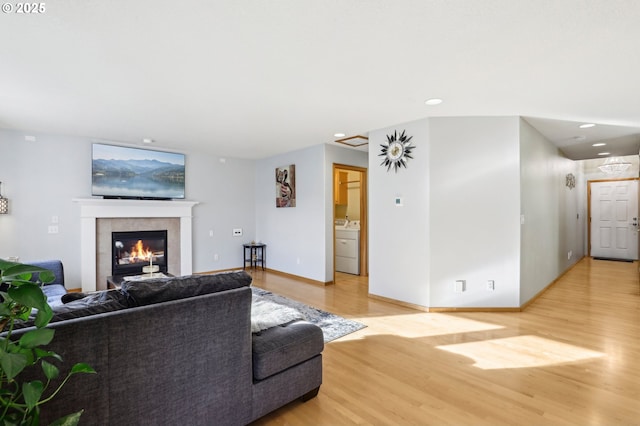 living room featuring a tiled fireplace, washer / dryer, and light hardwood / wood-style floors