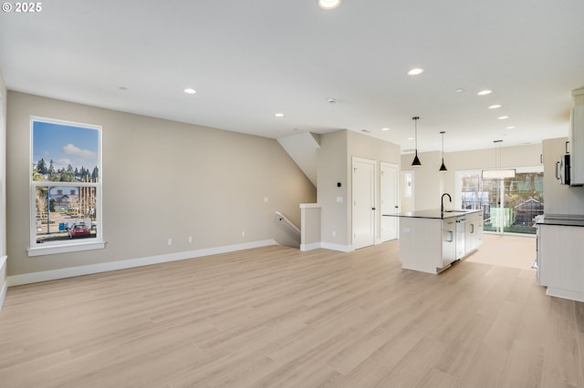 kitchen featuring dark countertops, light wood finished floors, a center island with sink, and white cabinets